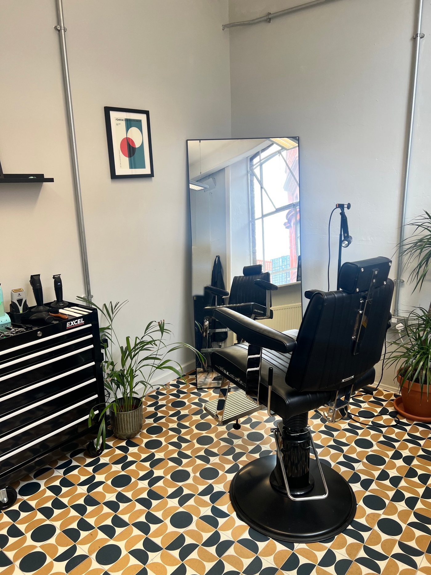 The FORME studio: black barber chair, full-length mirror, tool trolley and plants on a patterned tile floor
